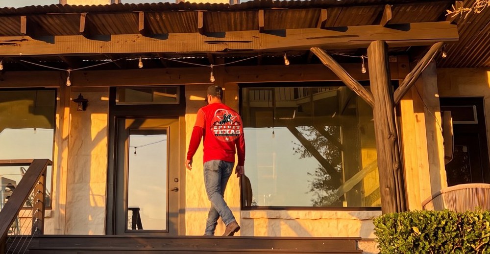 A Spirit of Texas crew member in a real logo shirt walking a finished porch at golden hour — the local crew behind the work.