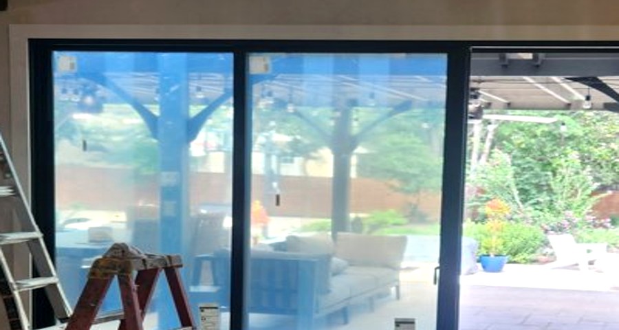 Close-up of a new sliding door frame's top corner on install day, protective film tabs still on the glass, from a real Spirit of Texas job.