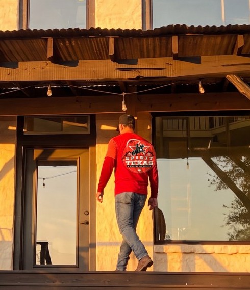 A Spirit of Texas crew member in a logo shirt walking a job-site porch at golden hour, Central Texas.