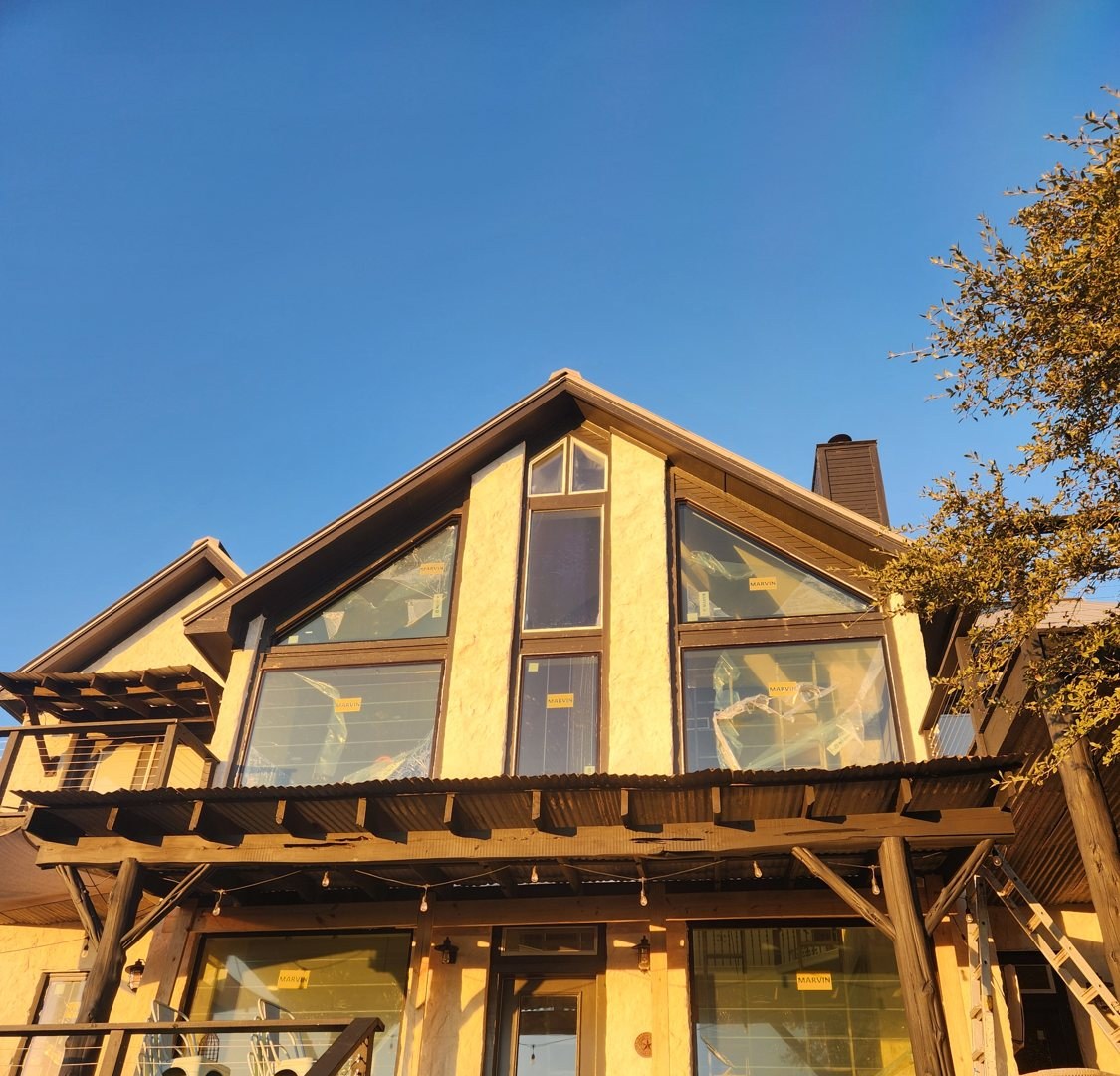 A Central-Texas ranch home at dusk with warm light glowing through crisp new windows, framed by live oaks.