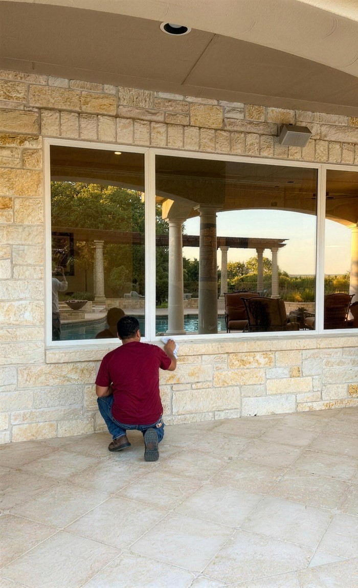 A Spirit of Texas installer checking and sealing a new picture window set into limestone, real job, Central Texas.