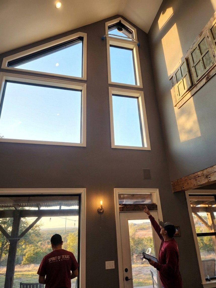 Mid-project walkthrough inside the same Hill Country home: a Spirit of Texas crew member in a real logo shirt checking the window wall.